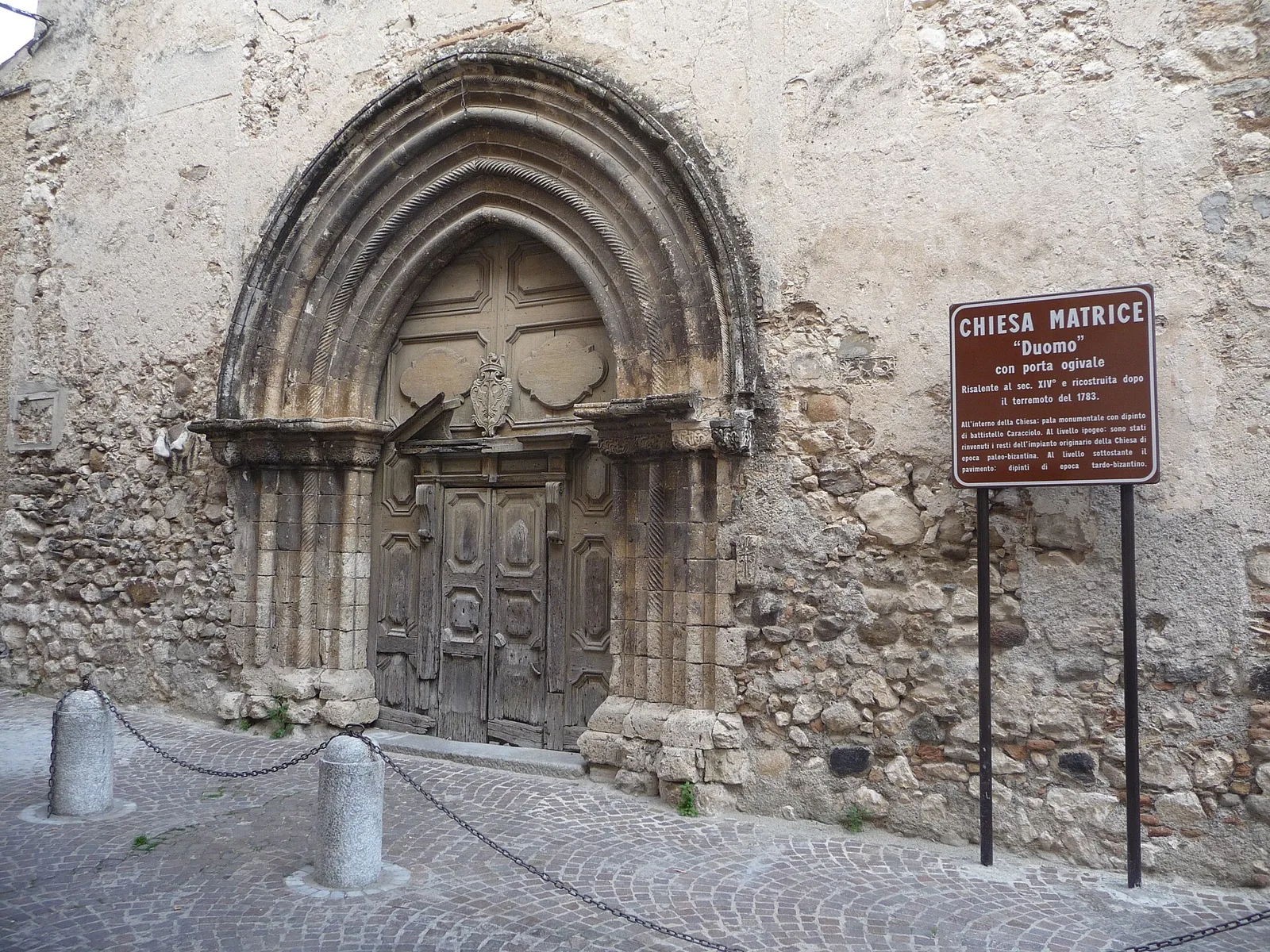 Gotycki portal Duomo w Stilo z tablicą informacyjną.